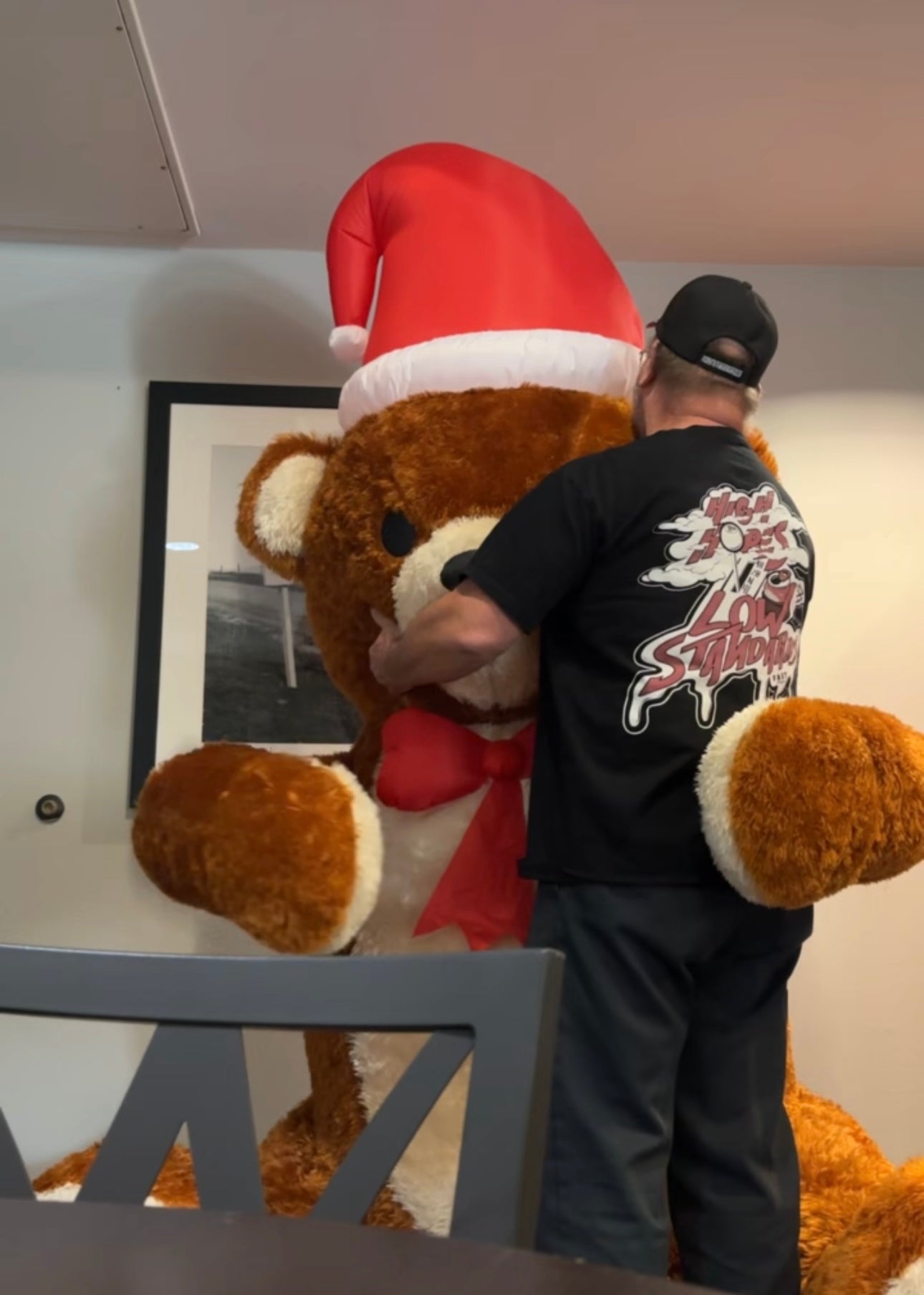 A person wearing a Fast Friends shirt  holding a large plush teddy bear wearing a Santa hat.